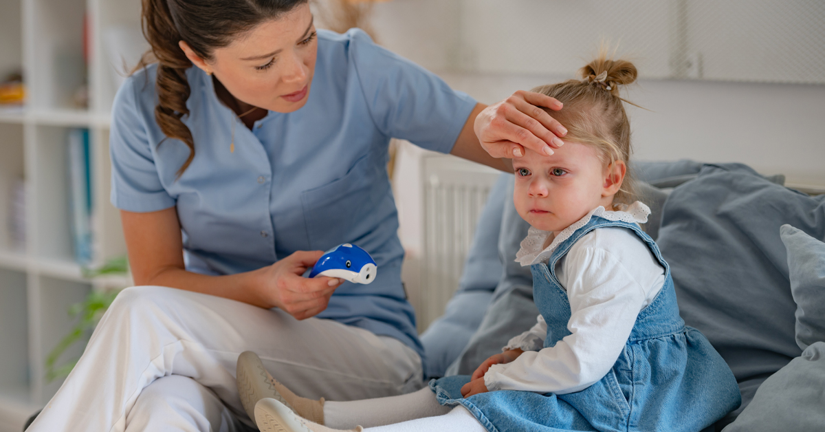 Thema: Kranke Kinder. Auf dem Bild ist ein krankes kleines Mädchen zu sehen. Eine Frau mit einem Fieberthermometer in der Hand sitzt neben ihr und hat die Hand auf der Stirn des Mädchens.