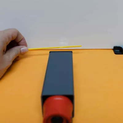 Plastiklineal, gelber Stab, orangefarbener Untergrund, Hand hält, Schlitzgerät