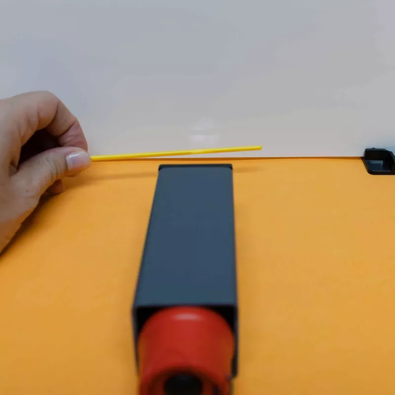 Plastiklineal, gelber Stab, orangefarbener Untergrund, Hand hält, Schlitzgerät